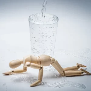 水が溢れ出ているガラスのコップと、手前で力尽きて倒れ込んでいる木製の人形。子どもの小さな受け皿と、情報過多による心身のオーバーヒートを表すイメージ