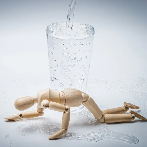 水が溢れ出ているガラスのコップと、手前で力尽きて倒れ込んでいる木製の人形。子どもの小さな受け皿と、情報過多による心身のオーバーヒートを表すイメージ